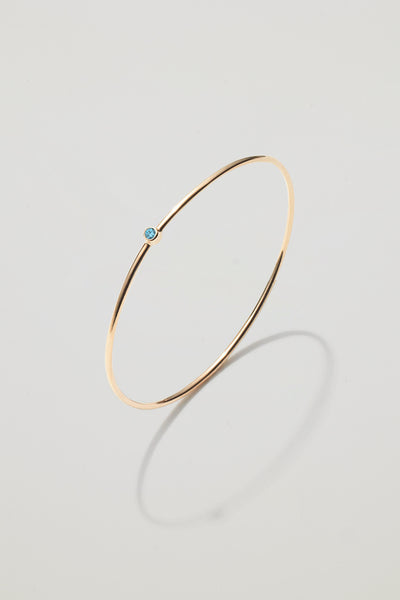 Solid gold bangle with a December blue topaz birthstone, symbolising peace and clarity.
