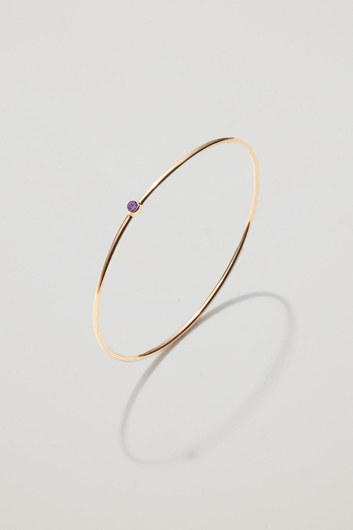 Solid gold bangle with a February amethyst birthstone, symbolising calm and clarity.
