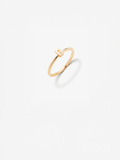 Close-up image of a personalised B  gold ring adorned with intricate, miniature dimensional letters from the alphabet on a light grey background 