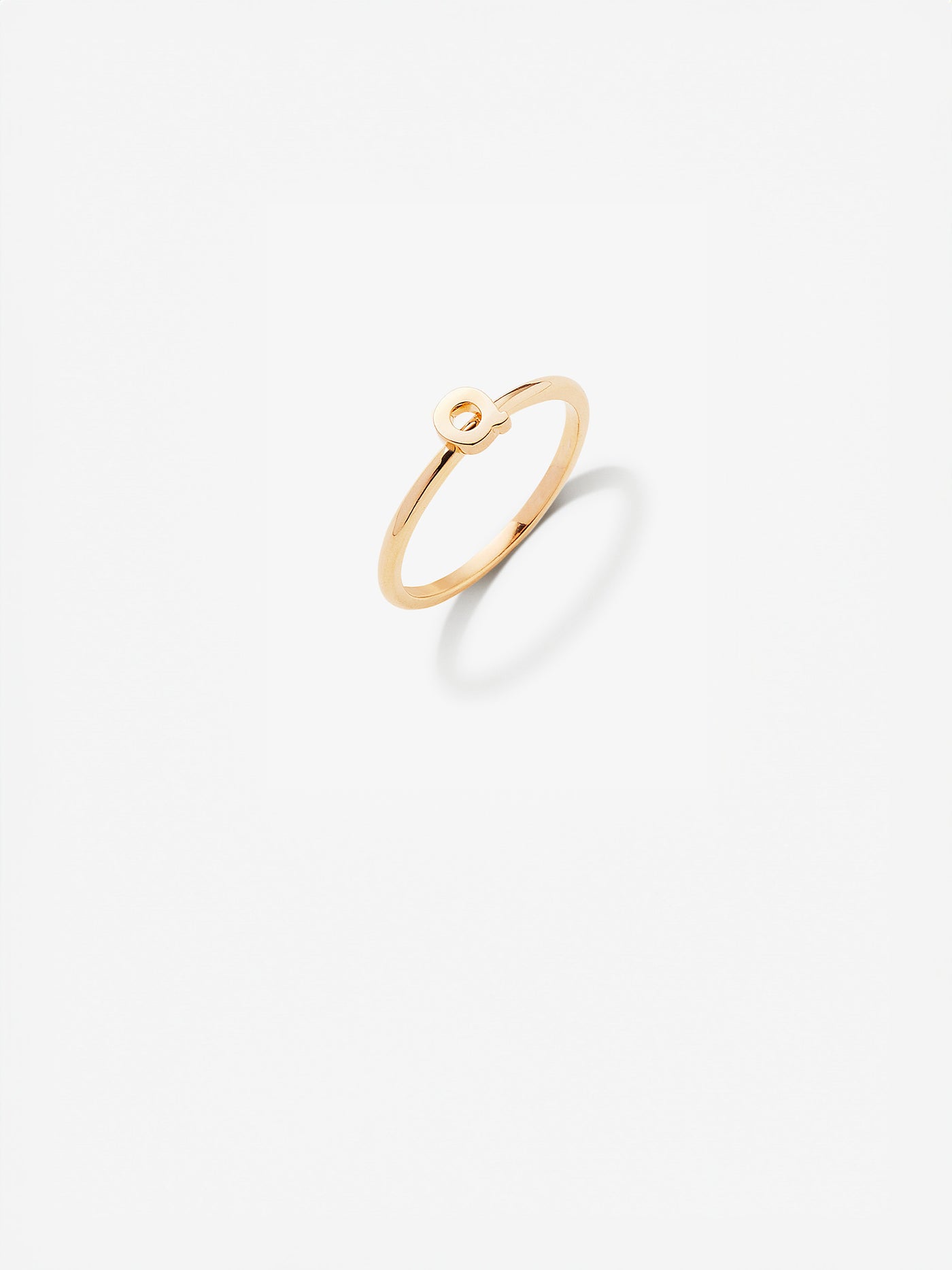 Close-up image of a personalised Q gold ring adorned with intricate, miniature dimensional letters from the alphabet on a light grey background 