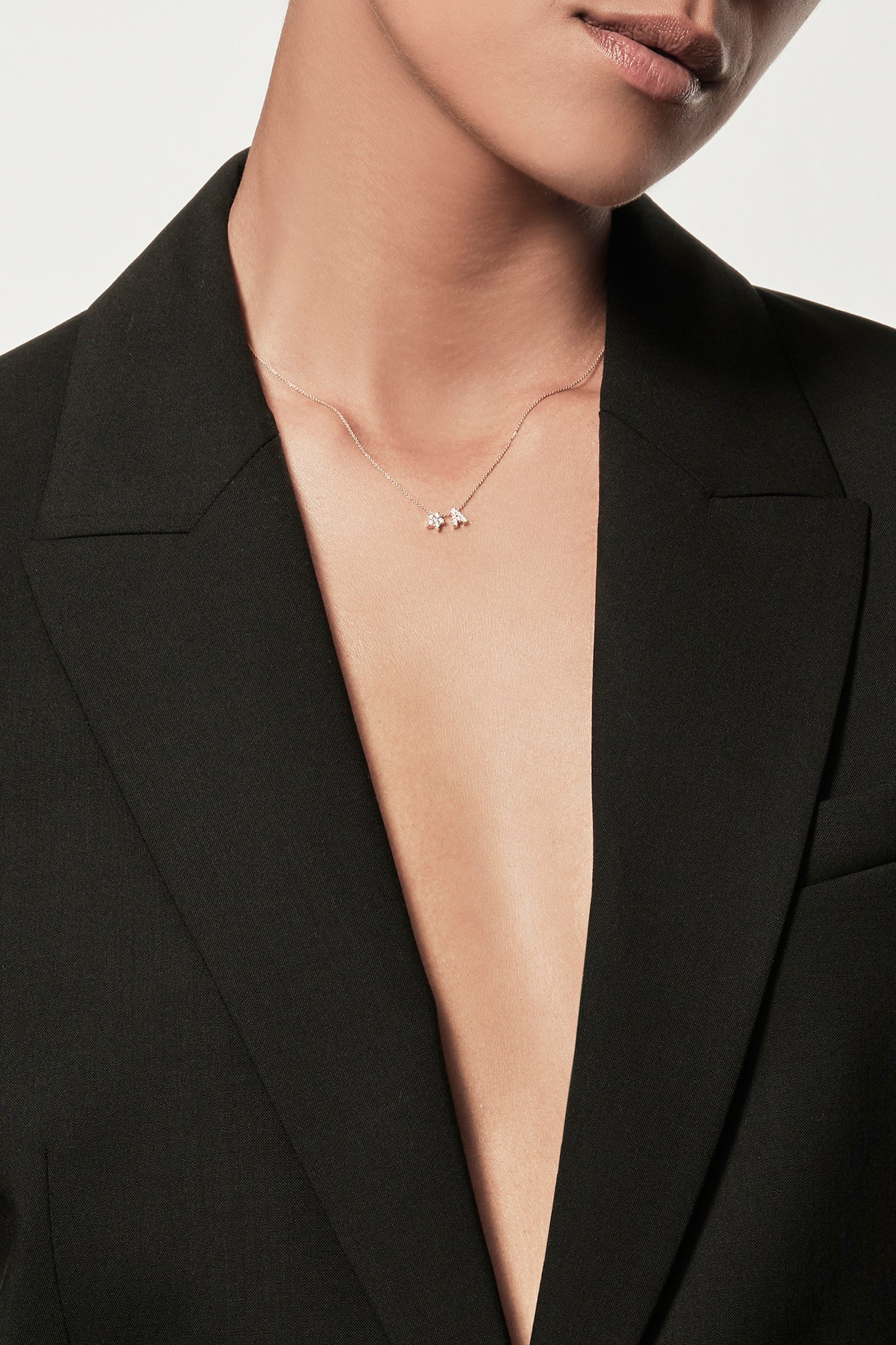 Close-up of a woman wearing a minimalist 18k gold diamond star necklace, styled with a black blazer, personalised alphabet pendant jewellery