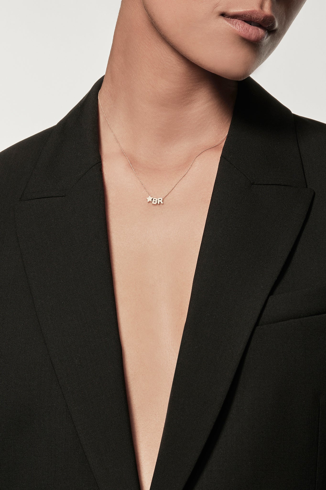 a necklace featuring three charms: the initials "B" and "R" separated by a small star charm all strung onto a fine chain with an openable connector clasp. The plain white background highlights the simplicity and elegance of this exquisite necklace.