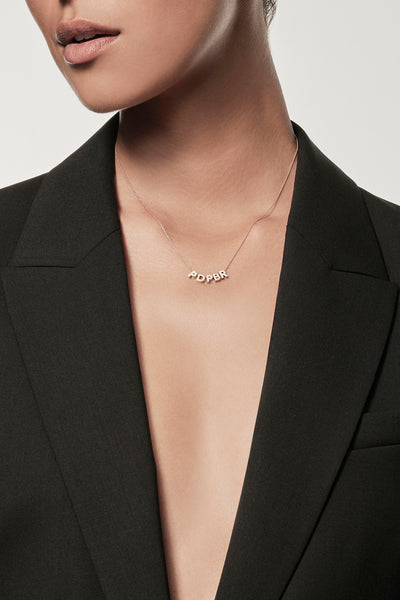 Close-up of a woman wearing a minimalist 18k gold initials “P" "D" "P" "B" "R" charms on a fine chain, styled with a black blazer – personalised alphabet pendant jewellery
