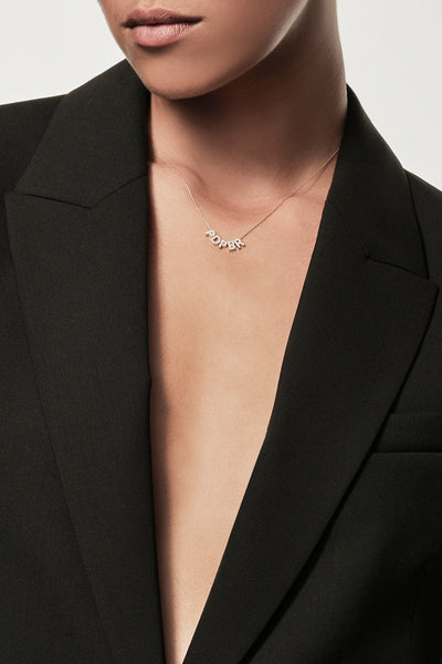 Close-up of a woman wearing a minimalist 18k gold and diamond initials “P” "D" "P" "B" "R" necklace, styled with a black blazer, personalised alphabet pendant jewellery