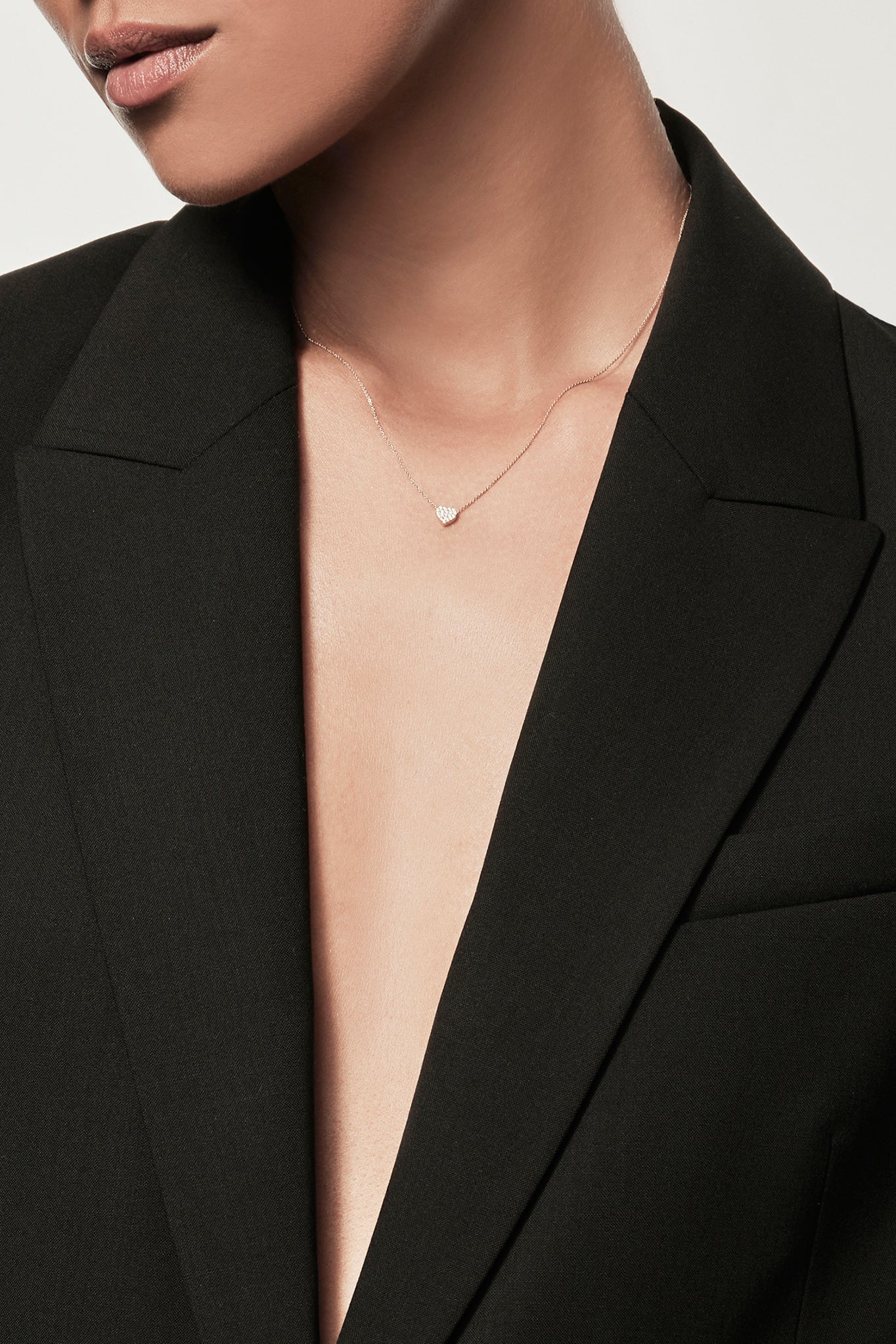 Close-up of a woman wearing a 18k gold diamond heart necklace, styled with a black blazer, personalised alphabet pendant jewellery